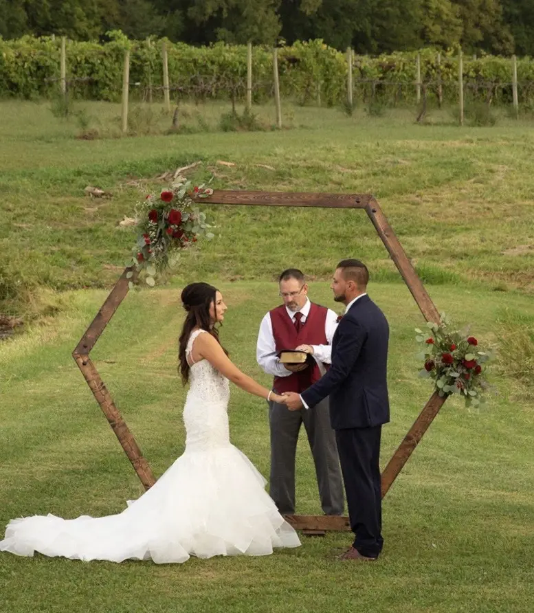 A couple getting married under an arch in the grass.